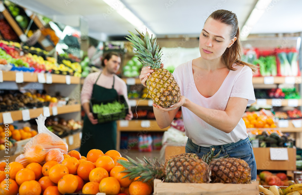 Young woman customer holding  fresh pineapples in hands