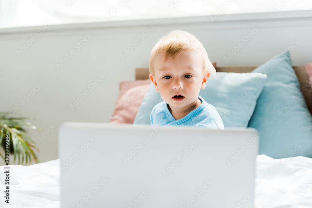 selective focus of surprised toddler kid looking at laptop in modern bedroom selective focus of surprised toddler kid looking at laptop in modern bedroom