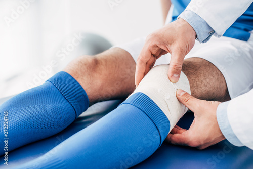partial view of Physiotherapist putting elastic bandage on leg of football player