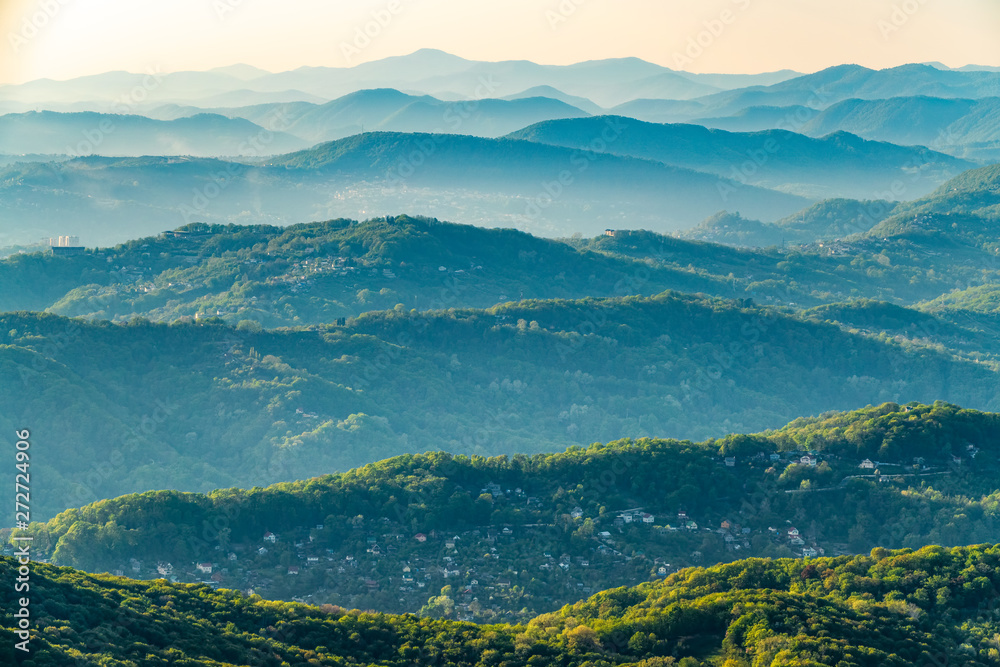 Fototapeta premium Layers of mountains in the haze during sunset. Beautiful sunset in the mountains. Beautiful sunset in a hilly valley with villages and fog in the lowlands.