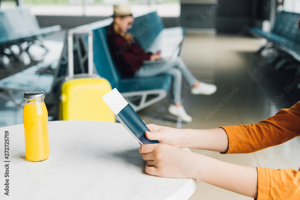 Cropped view of preteen kid holding passport and air ticket in airport on table with orange juice