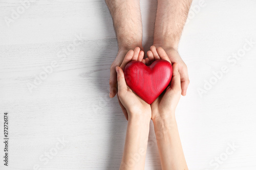 Couple holding decorative heart on white wooden background  top view