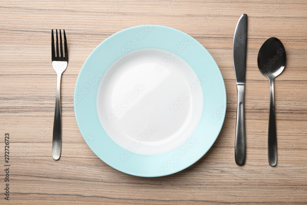 Stylish ceramic plate and cutlery on wooden background, flat lay Stylish ceramic plate and cutlery on wooden background, flat lay