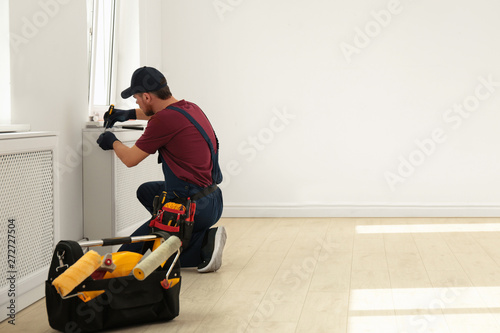 Handyman in uniform working with screwdriver indoors, space for text. Professional construction tools