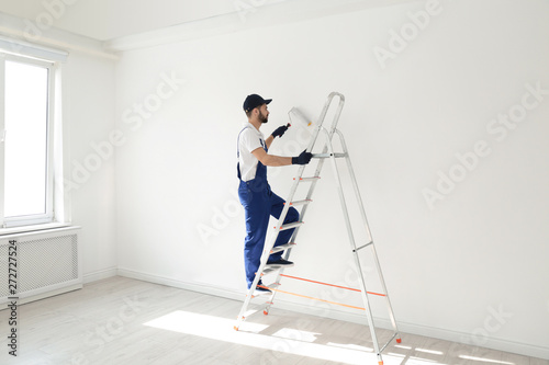 Handyman painting wall with roller brush indoors. Professional construction tools