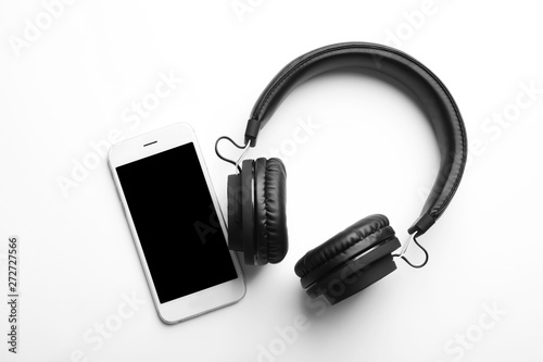 Stylish headphones and modern phone on white background, top view. Space for text