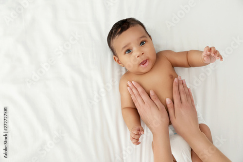 Top view of mother and her cute child on white bed, space for text. Baby massage and exercises