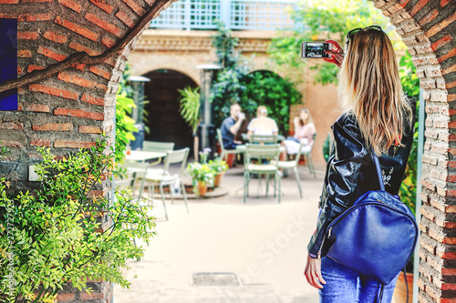 A girl with blond hair takes pictures of the sights on the phone, with her back to the camera. © Natallia