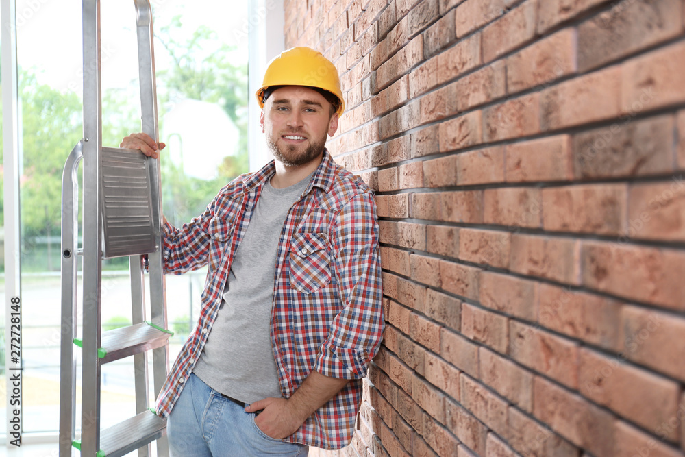 Young working man with ladder near brick wall. Space for text Young working man with ladder near brick wall. Space for text