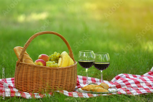 Wicker basket with food and wine on blanket in park  space for text. Summer picnic