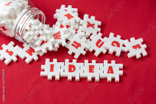 Business idea, creativity and imagination concept, abundance white puzzle jigsaw with alphabets combine word IDEA and other letter pieces pouring from glass bottle on red fabric background