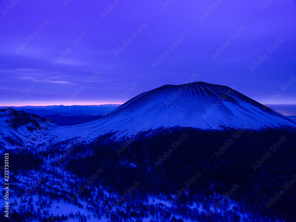 Fototapeta premium 峠から雪山を撮影、空は濃いブルー色の雲に覆われ遠くの地平線がほんのり朝焼け色に染まる、この山の特有な筋状の残雪模様が目を引く。