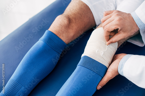cropped view of Physiotherapist putting elastic bandage on leg of football player