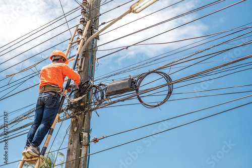 Electrical linemam worker climb a bamboo ladder to repair wire. A telecom engineer installing wire for internet.