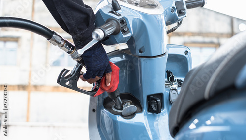 Close up of hand holding nozzle fuel filling oil into motorcycle front tank. Transportation and energy concept.