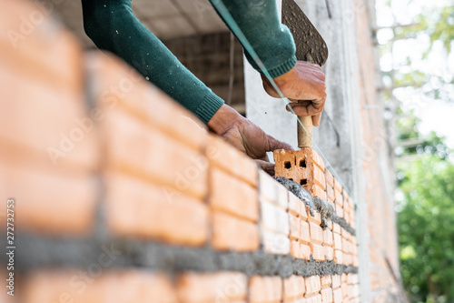 Close up of bricklayer worker's hand installing red brick with trowel putty knife for new house building at construction site.