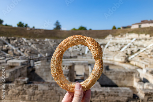 Fototapeta Naklejka Na Ścianę i Meble -  Hand holding a greek koulouri over the First Ancient Theater of Larissa as blur background in Greece.