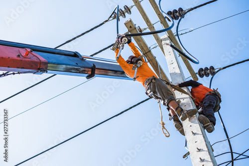 Two electrician workers are climbing on the electric poles to install and repair power lines.