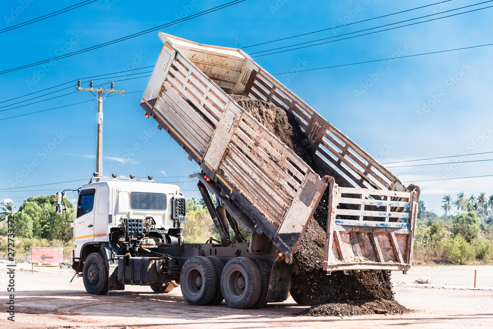 Back view of dump truck unloading soil or sand at construction site with blue sky.