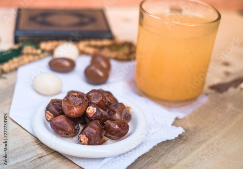 Date-palm in white plate with orange juice, small quran and rosary placed on wooden background. Simple iftar food set for Ramadan break fasting.