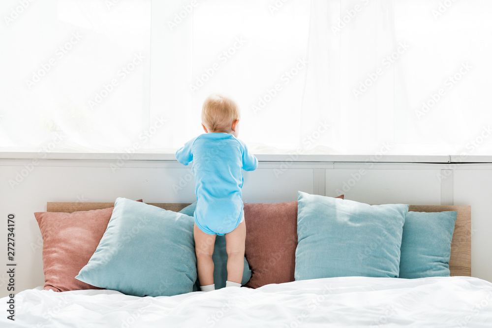 back view of toddler kid standing on bed and looking at window in bedroom back view of toddler kid standing on bed and looking at window in bedroom