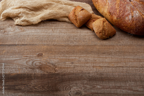 fresh bread loaf and buns near cloth on wooden table with copy space