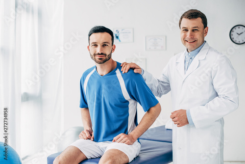smiling Physiotherapist and football player in hospital looking at camera
