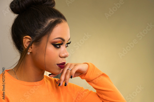 Portrait of attractive afro american young woman with fashion luxury makeup orange-coloured shades and her hair scraped back into high bun. Perfect Skin. Long eyelashes. Big lush beautiful lips. Side 