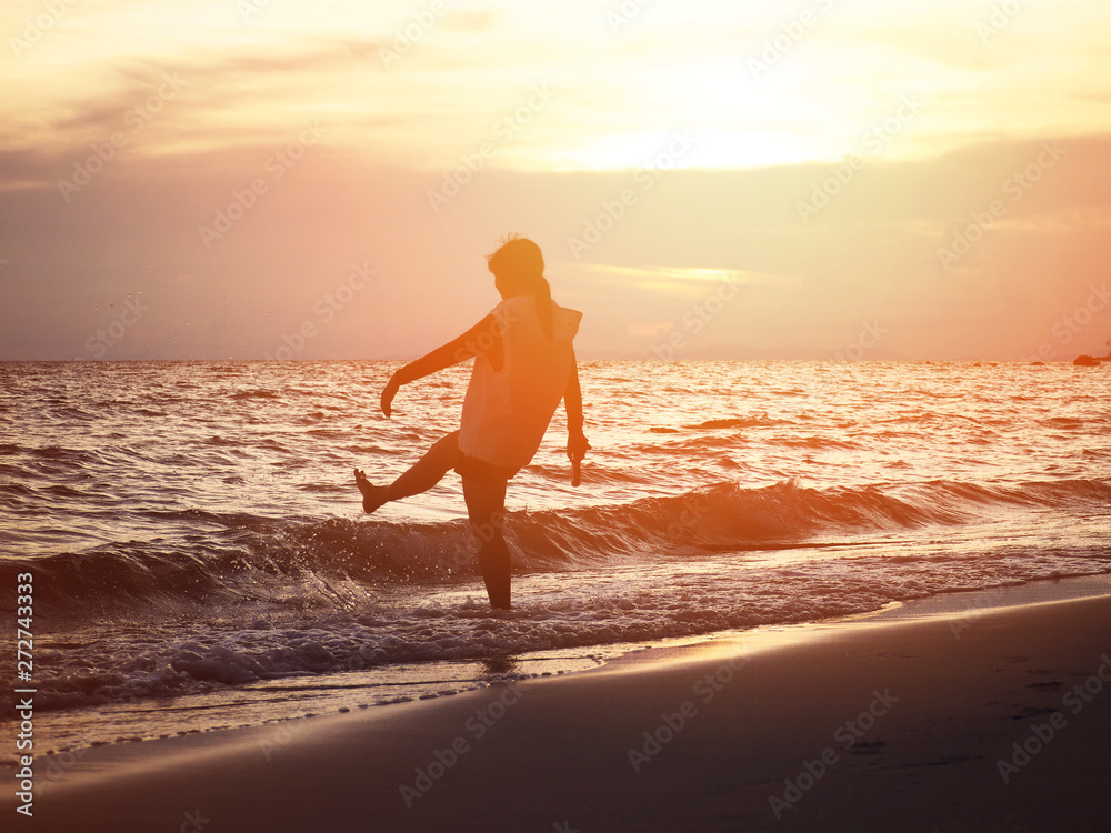 Silhouette smiling woman kicking water wave on the beach.