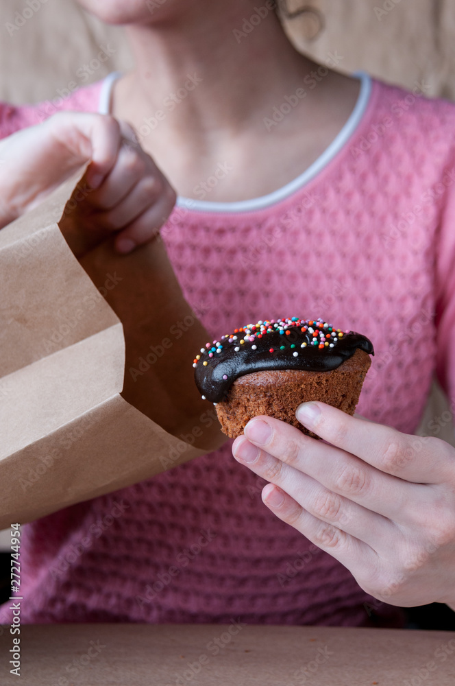 Fototapeta premium Girl in a pink blouse pulls out of a paper bag muffin with chocolate icing