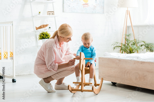 Photography cute toddler kid on wooden rocking horse near attractive blonde mother