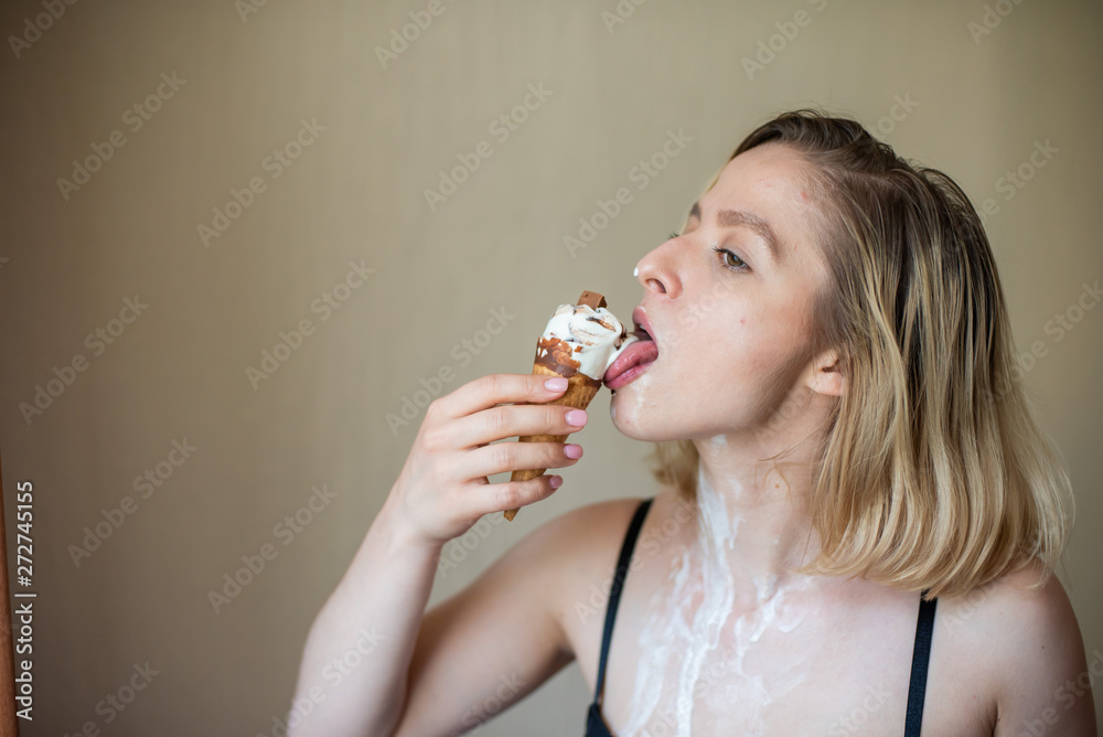 Sexy blonde licks a waffle cone. Ice cream is melting, erotically draining through the body of an attractive woman. Beautiful girl smeared with ice cream.