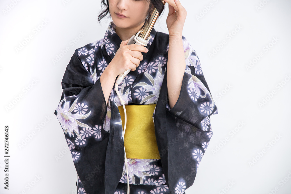 Foto Stock 浴衣を着た30代のきれいな女性が白背景でコテをつかってヘアセットしている Adobe Stock