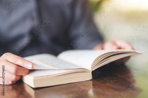 Closeup image of a woman holding and reading a vintage novel book on wooden table