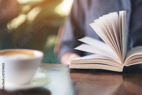 Closeup image of a woman holding and reading a book with coffee cup on wooden table