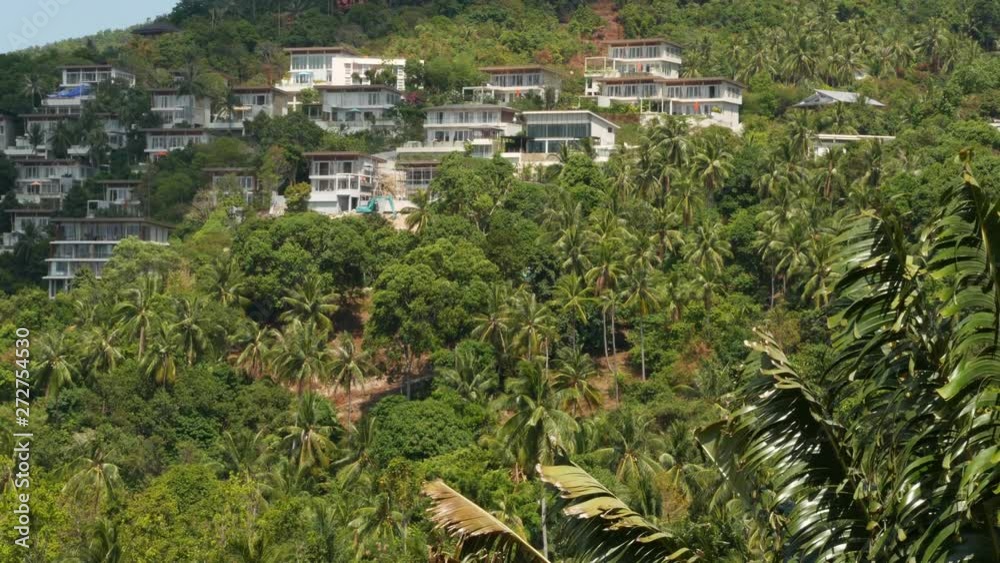 Luxury villas on mountain slope. Drone view of luxury houses located amidst exotic trees on green mountain on sunny day on tropical island Luxury villas on mountain slope. Drone view of luxury houses located amidst exotic trees on green mountain on sunny day on tropical island