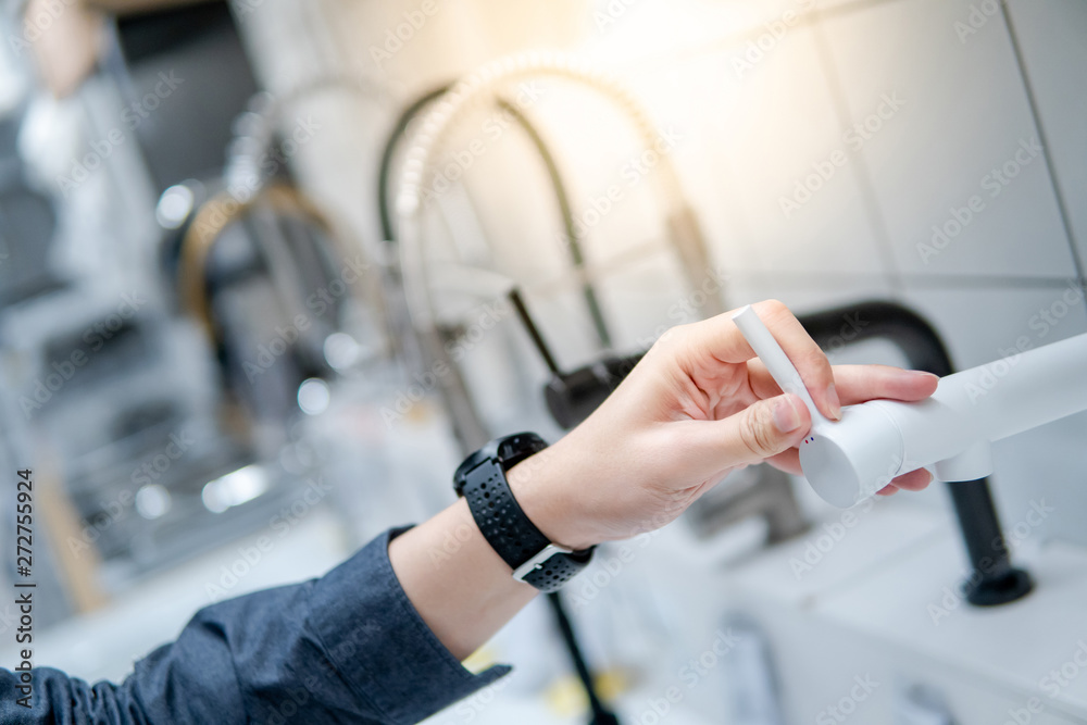 Male hand choosing modern white water tap in furniture store. Home improvement for domestic kitchen.