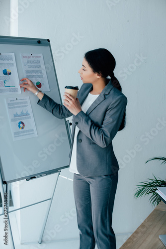 young latin businesswoman arranging infographics on flipchart while holding paper cup photo