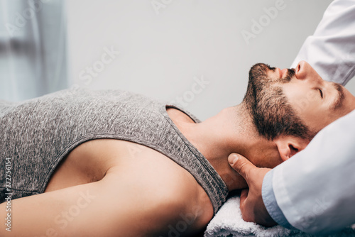 chiropractor massaging neck of man lying on towel in hospital
