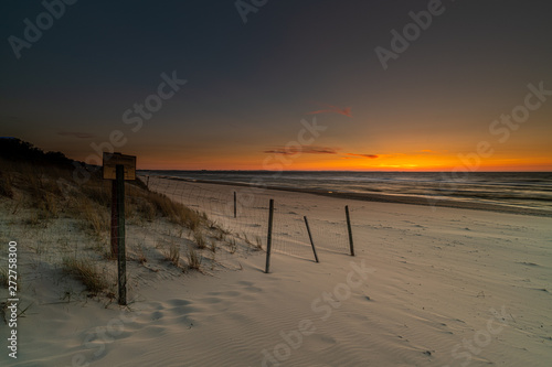 sandy beach with waved sea on colorful sunset background 