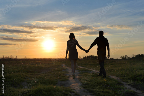 boy and girl go hand in hand on the field road to meet the sun