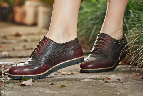 Women's leather boots close-up. The girl walks in shoes with a background of arrangeries with tropical plants. Oxford style shoes. © Ivan