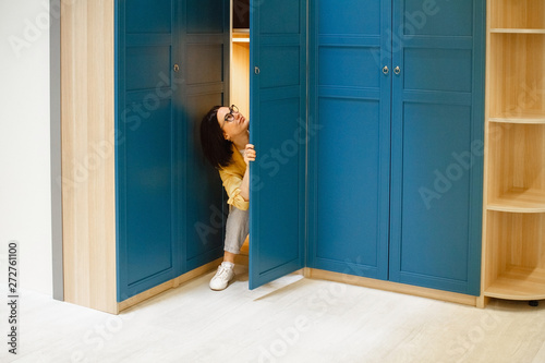 The concept of choice. The girl chooses a large, roomy closet in a furniture store. Peeking out of the closet