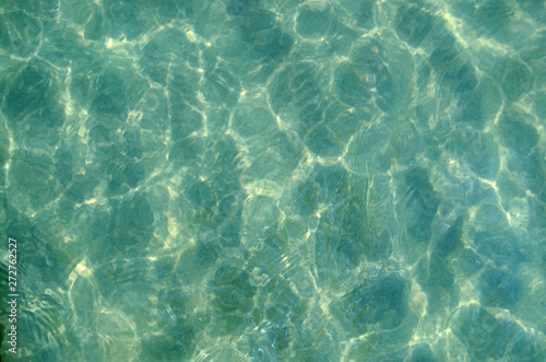 The sun pattern is a play of light and shadow in the form of highlights, spots and streaks on the calm clear surface of the emerald transparent sea water