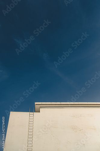 White wall and deep blue sky behind a ladder