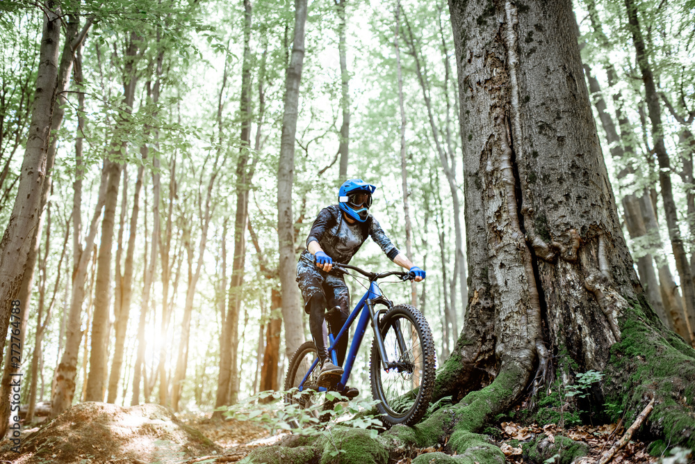 Naklejka premium Professional well equipped cyclist riding downhill on the off road in the forest. Concept of an extreme sport and enduro cycling