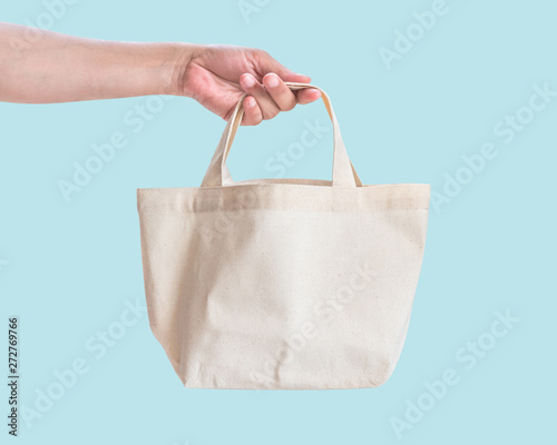 Tote bag canvas white cotton fabric cloth for eco shoulder shopping sack mockup blank template isolated on pastel blue background (clipping path) with woman’s hand handling handle straps