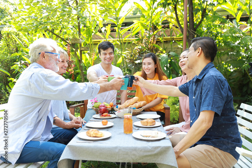 Happy multiethnic family sitting at a breakfast table in backyard outdoor on sunny day with smiling face while everyone clicking glasses.
