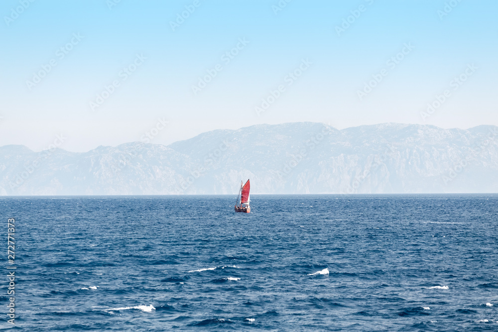 Sailboat with red sail at open sea. Long distant shot