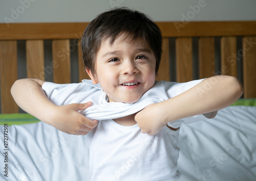 School boy sitting in bed and try to wearing his cloth with smiling face,Cute kid boy getting dressed and get ready for school,Child dressing uniform in bed room ready to school,Back to school concept